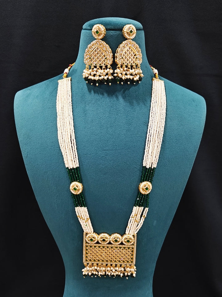 Close-up of an ornate traditional Green Rajwadi gold Long jewellery set and earrings with American Diamonds, Pearls, Crystal stones, Green colored stones. Close-up of a premium Rajwadi artificial necklace under 10000. Reception party look featuring a statement Rajwadi necklace.