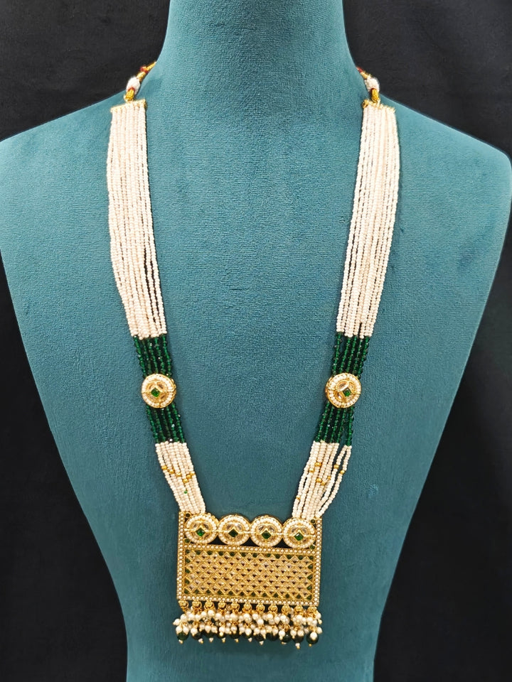 Close-up of an ornate traditional Green Rajwadi gold Long jewellery set and earrings with American Diamonds, Pearls, Crystal stones, Green colored stones. Close-up of a premium Rajwadi artificial necklace under 10000. Reception party look featuring a statement Rajwadi necklace.