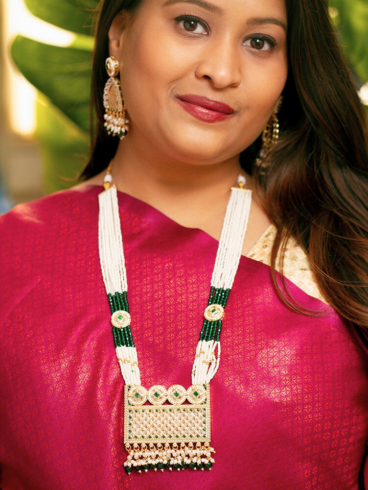 Close-up of a woman wearing an ornate traditional Green Rajwadi gold Long jewellery set and earrings with American Diamonds, Pearls, Crystal stones, Green colored stones. Woman styled in a royal Rajwadi artificial necklace set for a traditional Indian wedding. Reception party look featuring a statement Rajwadi necklace.