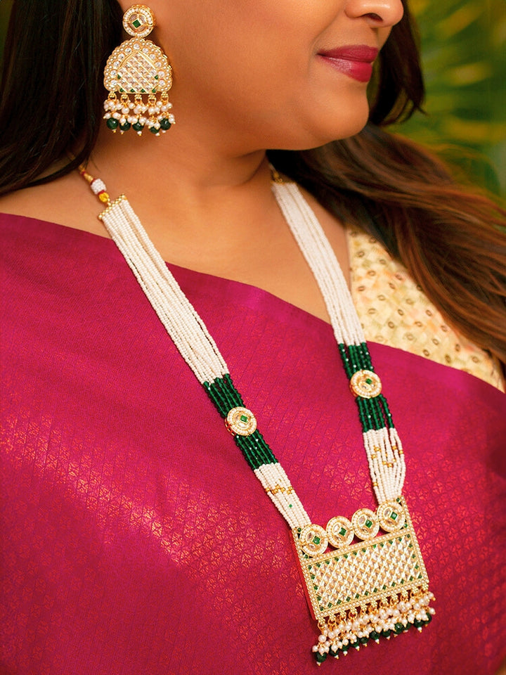 Close-up of a woman wearing an ornate traditional Green Rajwadi gold Long jewellery set and earrings with American Diamonds, Pearls, Crystal stones, Green colored stones. Woman styled in a royal Rajwadi artificial necklace set for a traditional Indian wedding. Reception party look featuring a statement Rajwadi necklace.