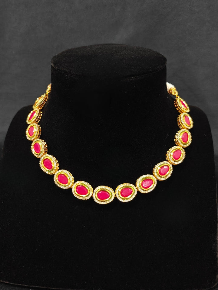 Close-up of an ornate traditional (Gold Polish) Pink Collar jewellery set and earrings with American Diamond and Pink Colored Stone. Festive Diwali outfit paired with a colorful Colored Stone necklace. Festive celebration look enhanced with traditional Colored Stone jewelry.