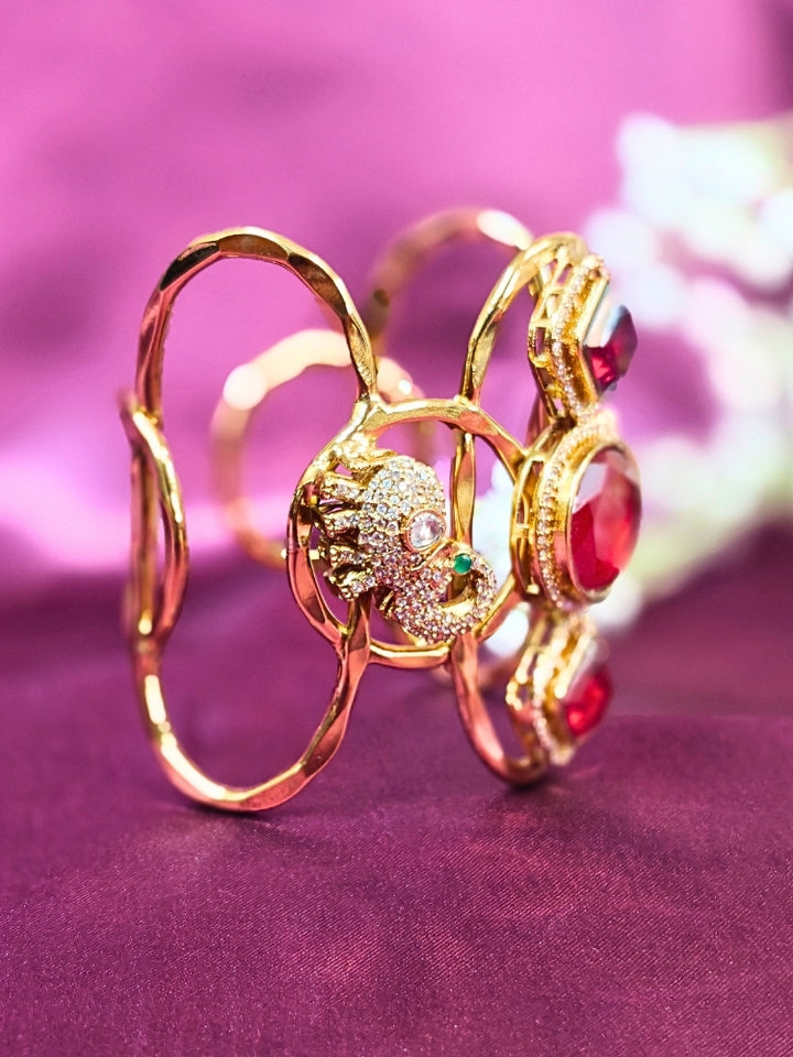 The Farah Red Bracelet (Adjustable) features intricate designs, three bold red gemstones, and two elephant heads adorned with American diamonds —ideal for wedding ceremonies—shown on a purple fabric background.
