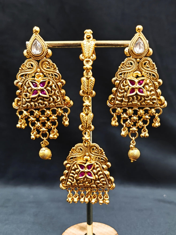 Close-up of an ornate traditional Heritage gold Choker jewellery set and earrings and maangtikka with Pink Colored tone. Luxury wedding styling featuring an antique-inspired artificial necklace. Traditional Indian bridal look completed with a heritage artificial jewelry set.