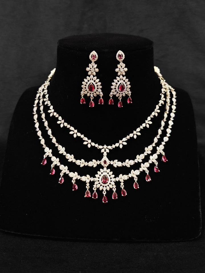 Close-up of an ornate Indo-Western Red American Diamond Silver Collar Layered jewellery set and earrings with American Diamond and Colored Stones. Bride-to-be styled in a premium American diamond artificial necklace for her reception party. Close-up of a bridal look featuring an anti-tarnish American diamond artificial necklace.