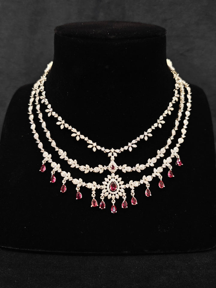 Close-up of an ornate Indo-Western Red American Diamond Silver Collar Layered jewellery set and earrings with American Diamond and Colored Stones. Bride-to-be styled in a premium American diamond artificial necklace for her reception party. Close-up of a bridal look featuring an anti-tarnish American diamond artificial necklace.