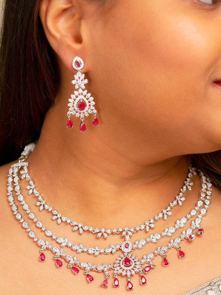 A stunning woman wearing a glamorous artificial diamond necklace with red colored stone paired with chic earrings, perfect for bridal wear. This high-quality artificial diamond jewelry set is the ideal choice for modern brides looking for a budget-friendly option with timeless sparkle.