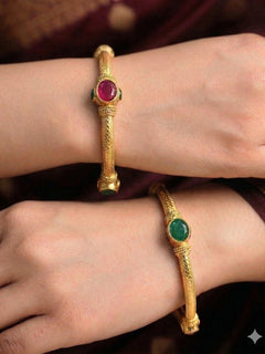 Close-up of a woman wearing an ornate traditional (Gold Polish) Bangles set with Red and Green Colored Stone. Festive celebration look enhanced with artificial Colored Stone bangles set. Festive Navratri outfit paired with stacked imitation Colored Stone bangles.