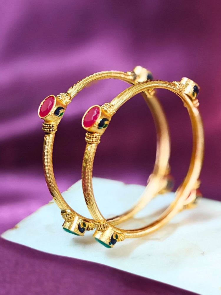 Close-up of an ornate traditional (Gold Polish) Bangles set with Red and Green Colored Stone. Festive celebration look enhanced with artificial Colored Stone bangles set. Festive Navratri outfit paired with stacked imitation Colored Stone bangles.