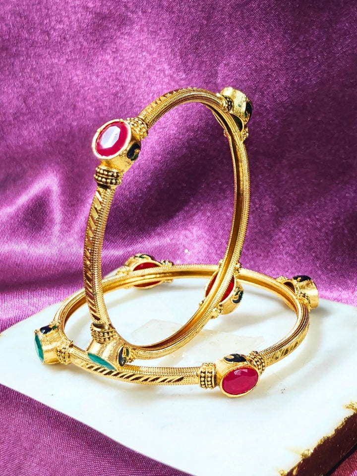 Close-up of an ornate traditional (Gold Polish) Bangles set with Red and Green Colored Stone. Festive celebration look enhanced with artificial Colored Stone bangles set. Festive Navratri outfit paired with stacked imitation Colored Stone bangles.