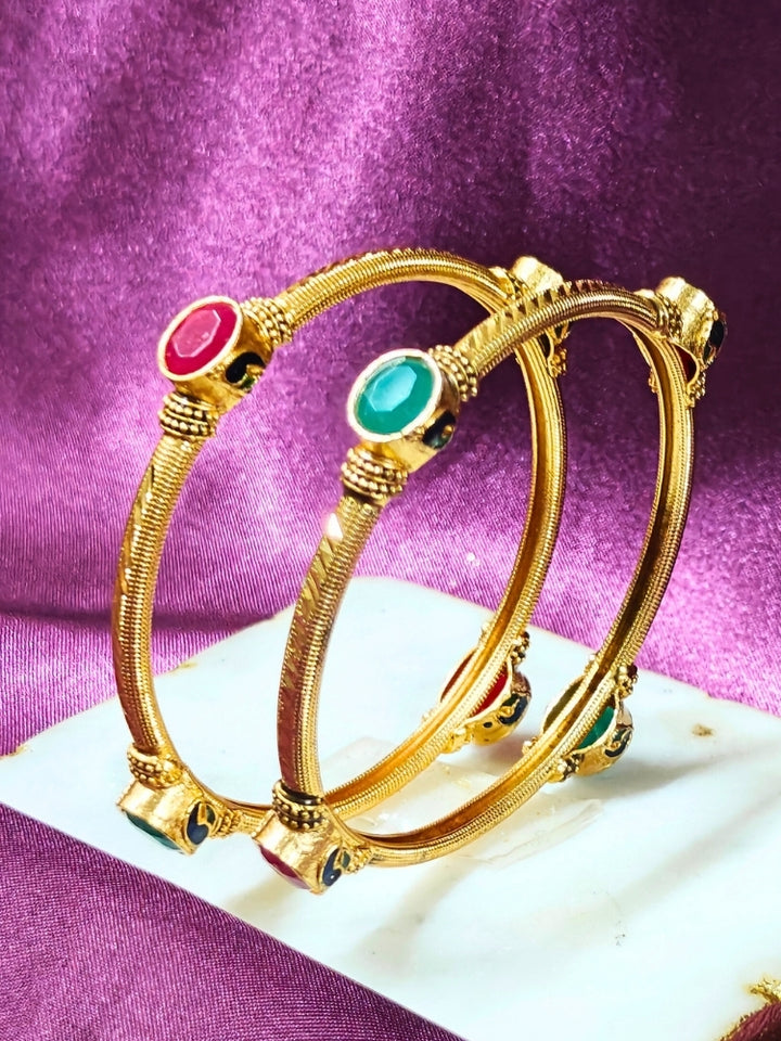 Close-up of an ornate traditional (Gold Polish) Bangles set with Red and Green Colored Stone. Festive celebration look enhanced with artificial Colored Stone bangles set. Festive Navratri outfit paired with stacked imitation Colored Stone bangles.