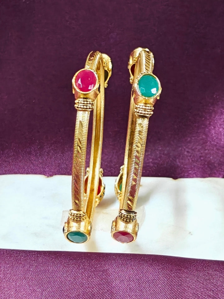 Close-up of an ornate traditional (Gold Polish) Bangles set with Red and Green Colored Stone. Festive celebration look enhanced with artificial Colored Stone bangles set. Festive Navratri outfit paired with stacked imitation Colored Stone bangles.