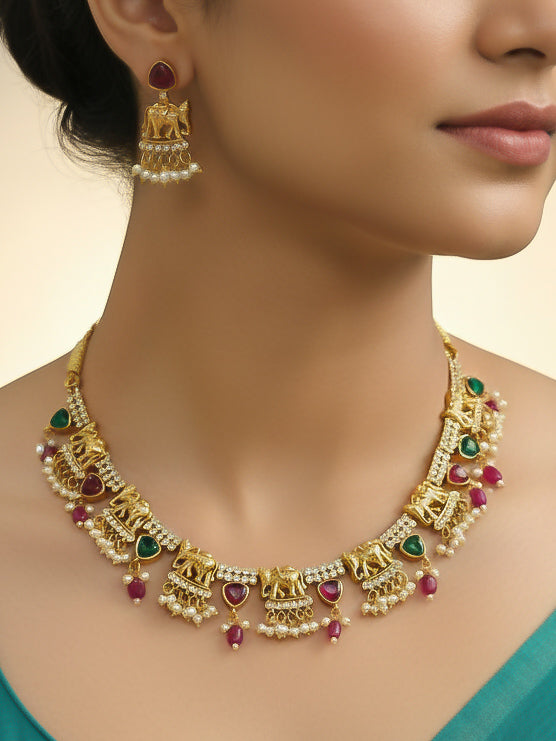 A woman wearing the Gajkesari Necklace Set featuring a traditional gold Collar Pink & Green necklace and matching earrings with pink and green colored stones, golden elephants and American Diamond. Close-up of a handcrafted temple imitation necklace styled with a silk saree. Woman wearing a temple-inspired artificial jewelry set for festive celebrations.