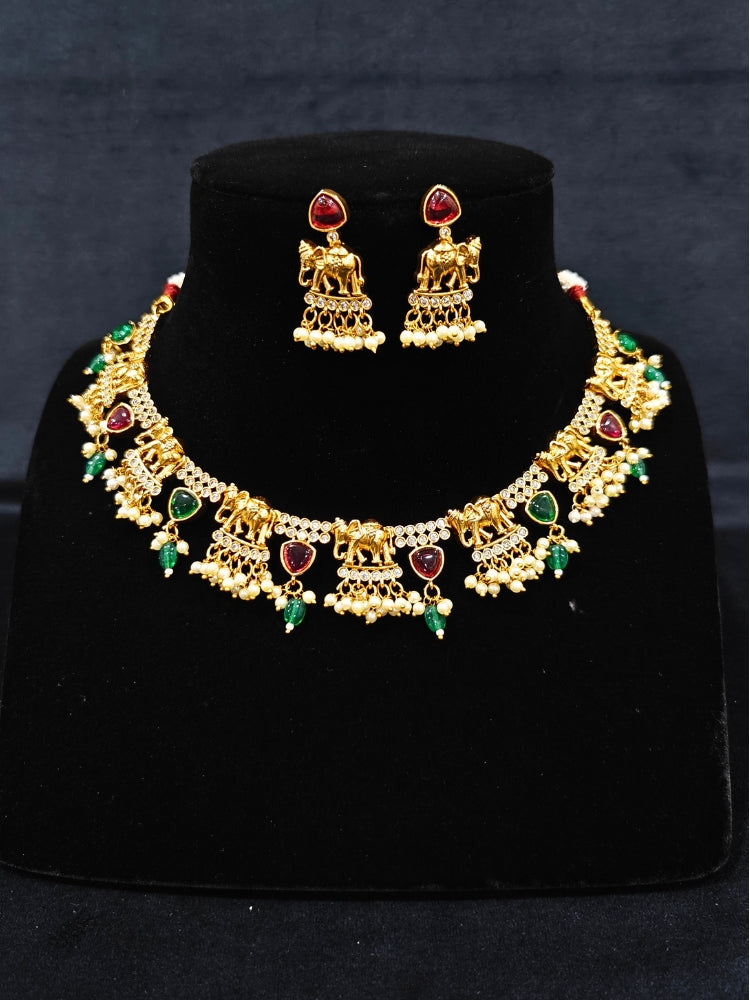 The Gajkesari Necklace Set featuring a traditional gold Collar Pink & Green necklace and matching earrings with pink and green colored stones, golden elephants and American Diamond. Close-up of a handcrafted temple imitation necklace styled with a silk saree. 