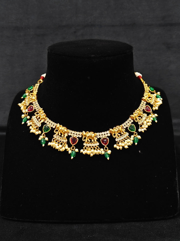 The Gajkesari Necklace Set featuring a traditional gold Collar Pink & Green necklace and matching earrings with pink and green colored stones, golden elephants and American Diamond. Close-up of a handcrafted temple imitation necklace styled with a silk saree. 