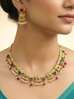A woman wearing the Gajkesari Necklace Set featuring a traditional gold Collar Pink & Green necklace and matching earrings with pink and green colored stones, golden elephants and American Diamond. Close-up of a handcrafted temple imitation necklace styled with a silk saree. Woman wearing a temple-inspired artificial jewelry set for festive celebrations.
