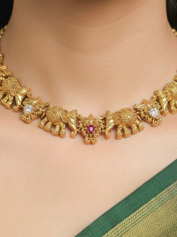 A woman wearing the Gajvani Red & White Necklace Set featuring a traditional gold collar necklace and matching earrings along with Red & White colored stones, golden elephants, paired with saree—ideal party jewelry for any festive occasion. Festive Diwali look completed with a traditional temple necklace set.