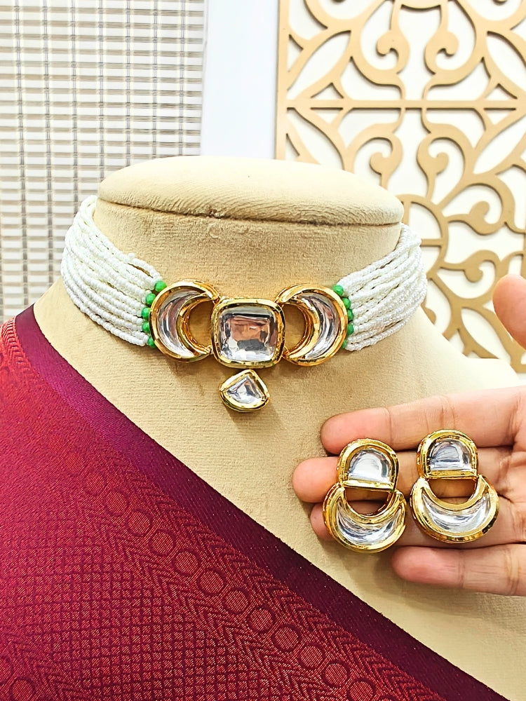 A mannequin wears the Gautami Choker Necklace Set—made with multiple strands of pearls along with kundan center design, with matching earrings —held by a hand and draped in luxurious maroon textured fabric.