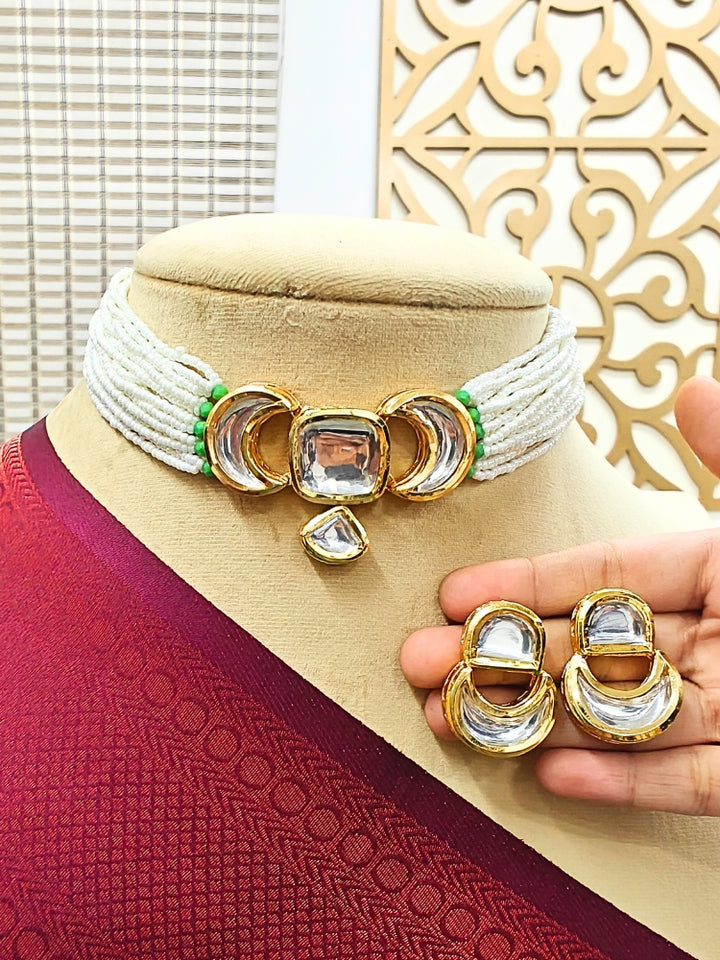 A mannequin wears the Gautami Choker Necklace Set—made with multiple strands of pearls along with kundan center design, with matching earrings —held by a hand and draped in luxurious maroon textured fabric.