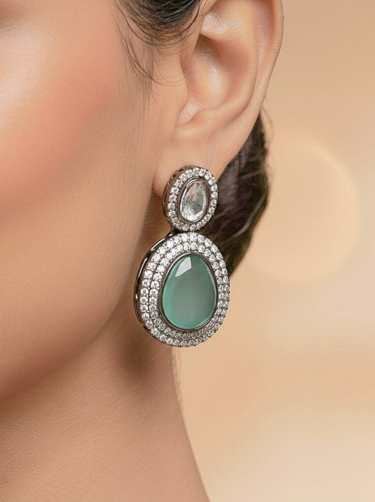 A woman with brown hair down smiles to the side, wearing the Teel Green Elizabeth Necklace Set featuring a statement Victorian-style necklace and matching earrings with large colorful stones, paired with a sparkly dark top.