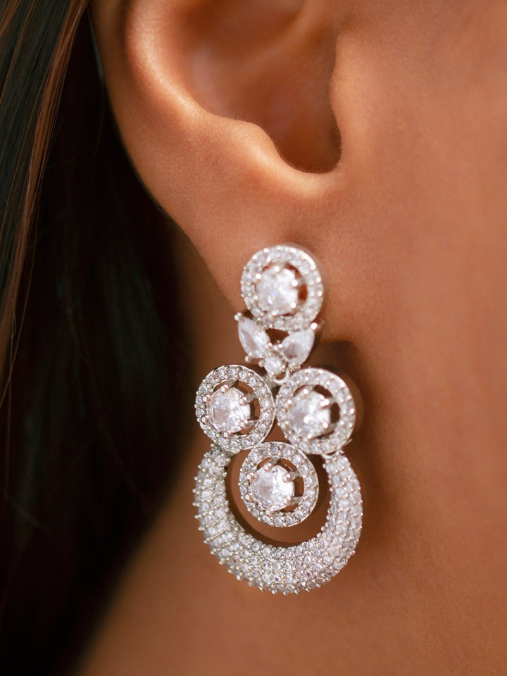 The Genevieve Necklace Set includes a sparkling silver necklace with matching earrings and a pendant, all adorned with circular American Diamonds and elegantly presented on black velvet against a gold satin fabric background.