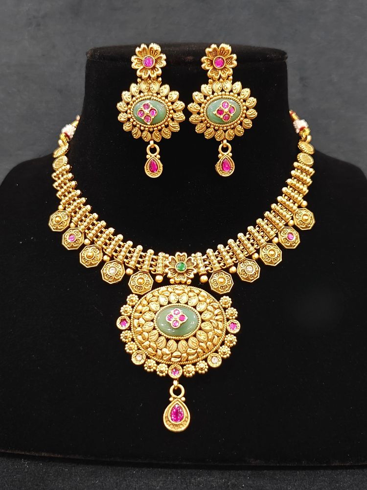 Close-up of an ornate traditional Heritage gold Collar jewellery set and earrings with Mint Green Colored Stones. Festive celebration outfit paired with a   handcrafted heritage jewelry set. Festive Diwali outfit styled with a royal heritage necklace.