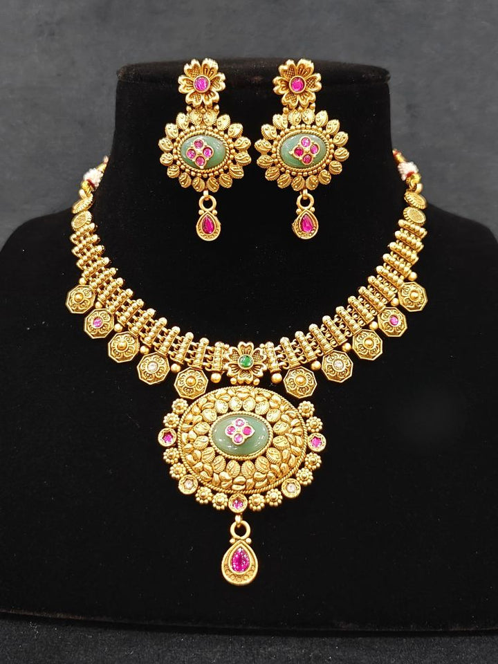 Close-up of an ornate traditional Heritage gold Collar jewellery set and earrings with Mint Green Colored Stones. Festive celebration outfit paired with a   handcrafted heritage jewelry set. Festive Diwali outfit styled with a royal heritage necklace.