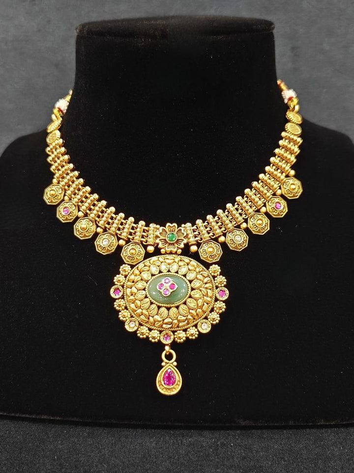 Close-up of an ornate traditional Heritage gold Collar jewellery set and earrings with Mint Green Colored Stones. Festive celebration outfit paired with a   handcrafted heritage jewelry set. Festive Diwali outfit styled with a royal heritage necklace.