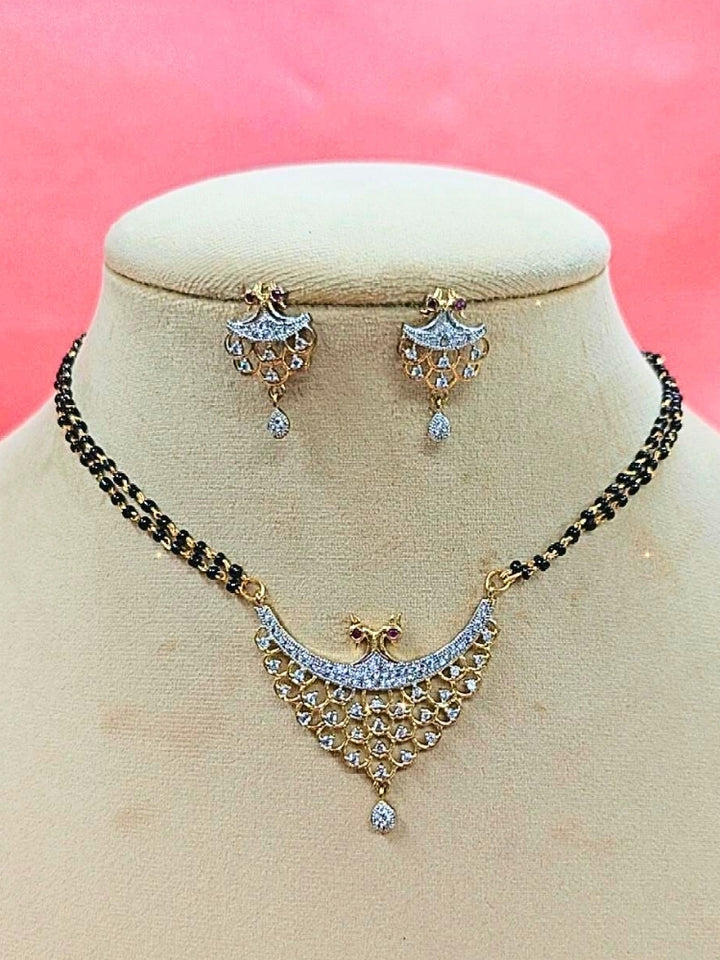 Gita Mangalsutra—a gold necklace with black mangalsutra beads and matching earrings, pendant featuring sparkling American Diamonds—set against a cream dummy, perfect for your wedding ceremony dress. Diamond mangalsutra. Modern mangalsutra. 
