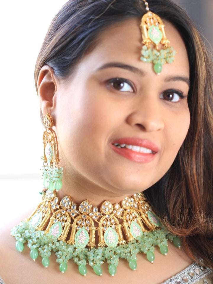 A woman with long dark hair wears the Green Jodha Necklace Set, featuring a heavy green Kundan Meena necklace with kundan, matching ornate earrings, and maangtikka. She smiles softly at the camera. Perfect meenakari kundan necklace for weddings. 