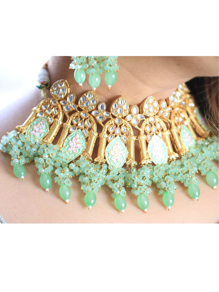A woman with long dark hair wears the Green Jodha Necklace Set, featuring a heavy green Kundan Meena necklace with kundan, matching ornate earrings, and maangtikka. She smiles softly at the camera. Perfect meenakari kundan necklace for weddings. 
