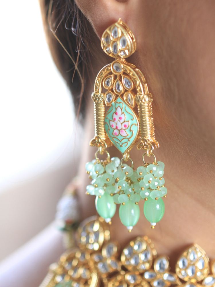 A woman with long dark hair wears the Green Jodha Necklace Set, featuring a heavy green Kundan Meena necklace with kundan, matching ornate earrings, and maangtikka. She smiles softly at the camera. Perfect meenakari kundan necklace for weddings. 