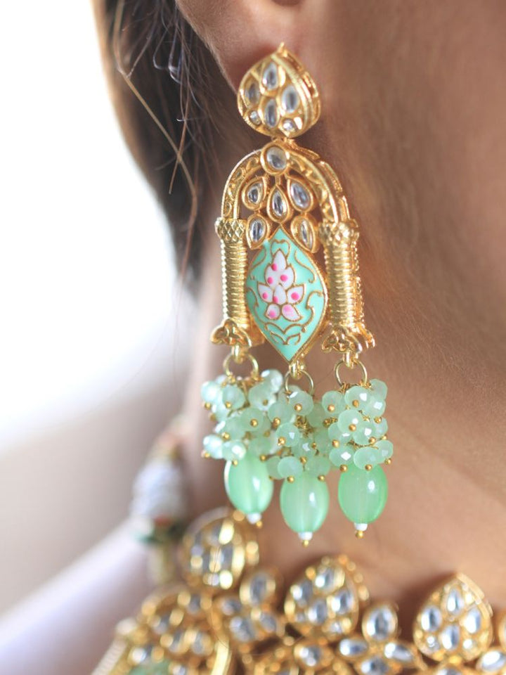 A woman with long dark hair wears the Green Jodha Necklace Set, featuring a heavy green Kundan Meena necklace with kundan, matching ornate earrings, and maangtikka. She smiles softly at the camera. Perfect meenakari kundan necklace for weddings. 