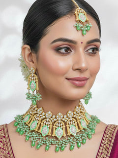 Close-up of a woman wearing an ornate traditional (Gold Polish) Green Choker jewellery set and earrings and maangtikka with Kundan, Meenakari, Crystal beads and Tumble beads. Close-up of intricate Kundan craftsmanship in artificial bridal jewelry. Bride wearing a traditional Kundan artificial necklace set for her wedding ceremony.