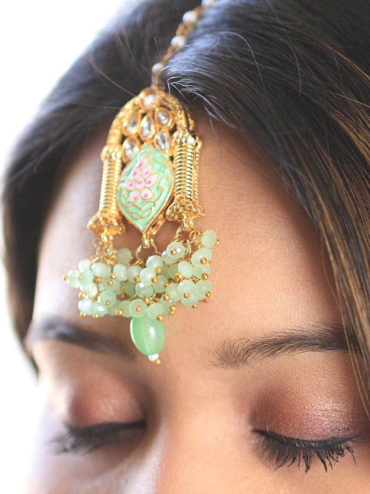 Close-up of a women wearing an ornate traditional (Gold Polish) Green Choker jewellery set and earrings and maangtikka with Kundan, Meenakari, Crystal beads and Tumble beads. Close-up of intricate Kundan craftsmanship in artificial bridal jewelry. Bride wearing a traditional Kundan artificial necklace set for her wedding ceremony.