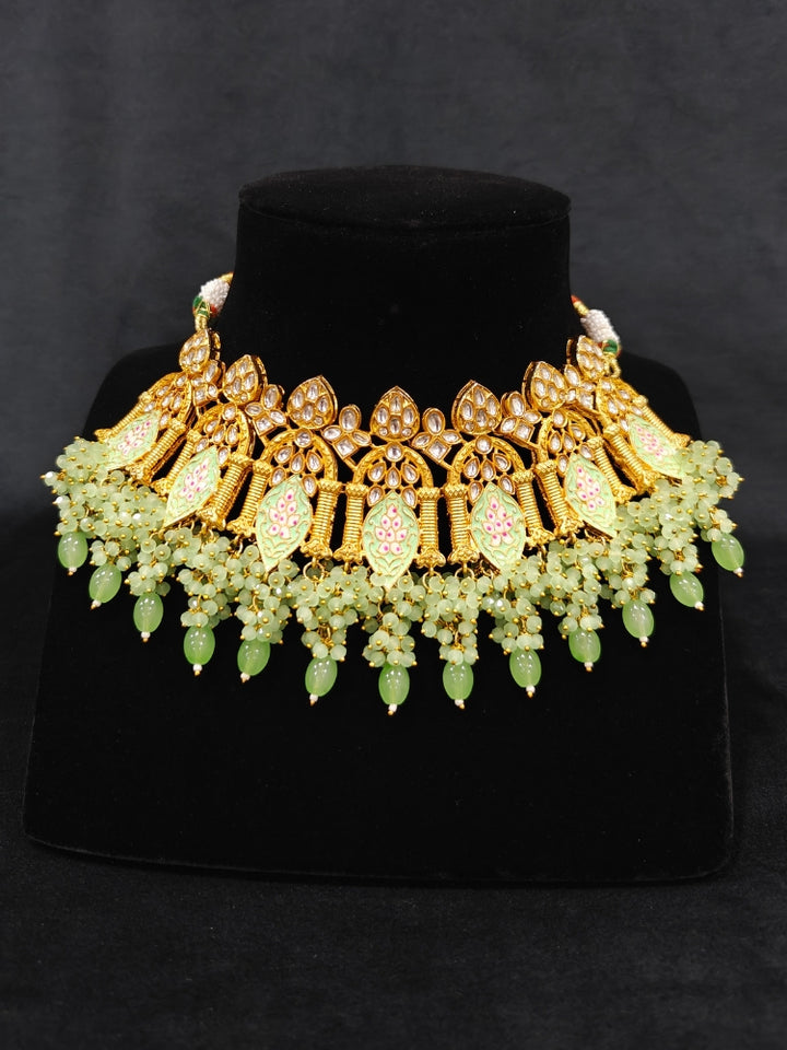 Close-up of an ornate traditional (Gold Polish) Green Choker jewellery set and earrings and maangtikka with Kundan, Meenakari, Crystal beads and Tumble beads. Close-up of intricate Kundan craftsmanship in artificial bridal jewelry. Bride wearing a traditional Kundan artificial necklace set for her wedding ceremony.