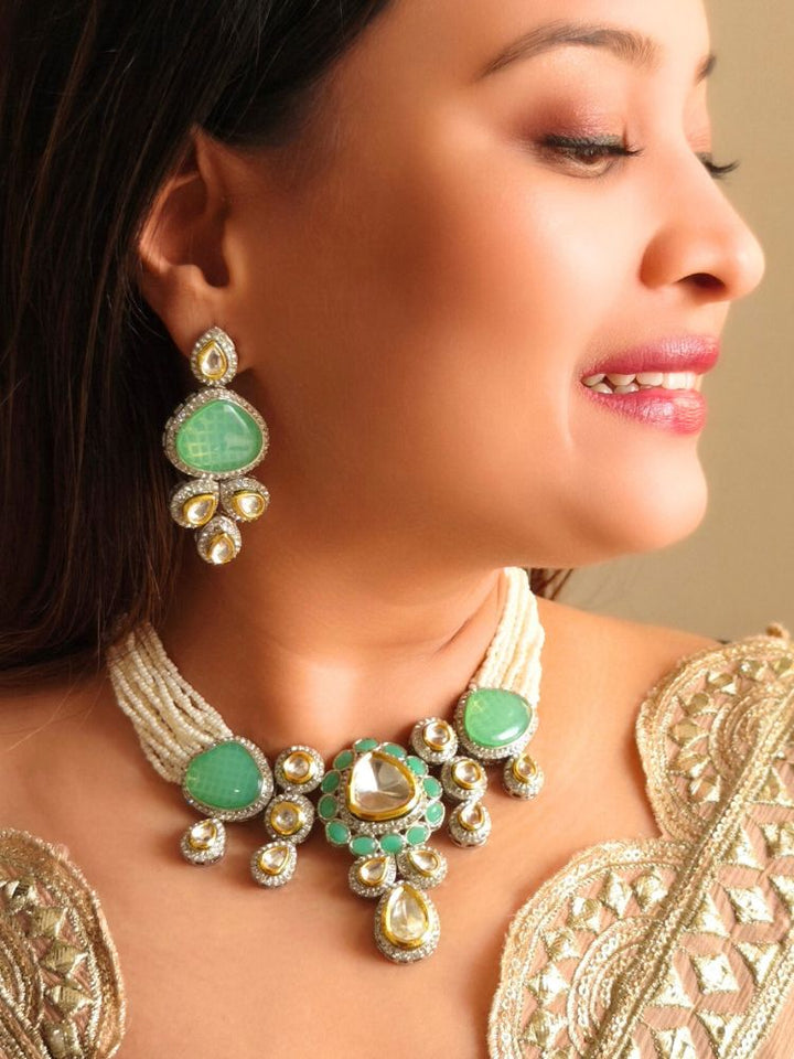 A woman in a gold embroidered outfit smiles, showcasing the Peacoski Green Tamanna Necklace Set and matching earrings. Her soft makeup highlights the elegance of this statement jewelry ensemble.