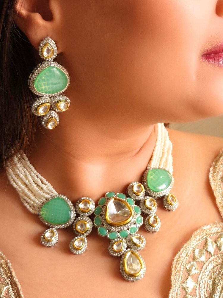 A woman in a gold embroidered outfit smiles, showcasing the Peacoski Green Tamanna Necklace Set and matching earrings. Her soft makeup highlights the elegance of this statement jewelry ensemble.