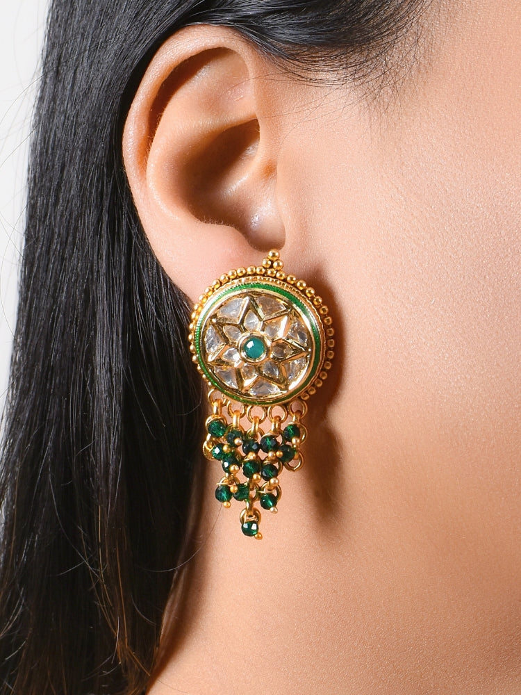 A close-up of a womans ear wearing Green Vartika Earrings—large, round gold earrings with tyani kundan, dangling green crystal beads, and American Diamond Polki—perfectly detailed for a wedding ceremony dress.