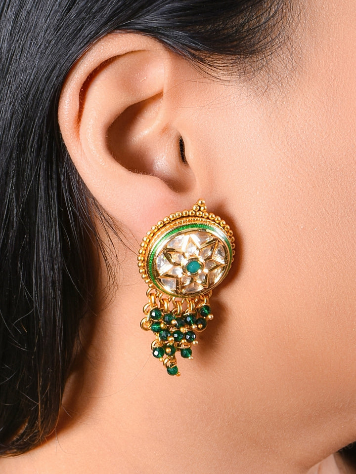 A close-up of a womans ear wearing Green Vartika Earrings—large, round gold earrings with tyani kundan, dangling green crystal beads, and American Diamond Polki—perfectly detailed for a wedding ceremony dress.