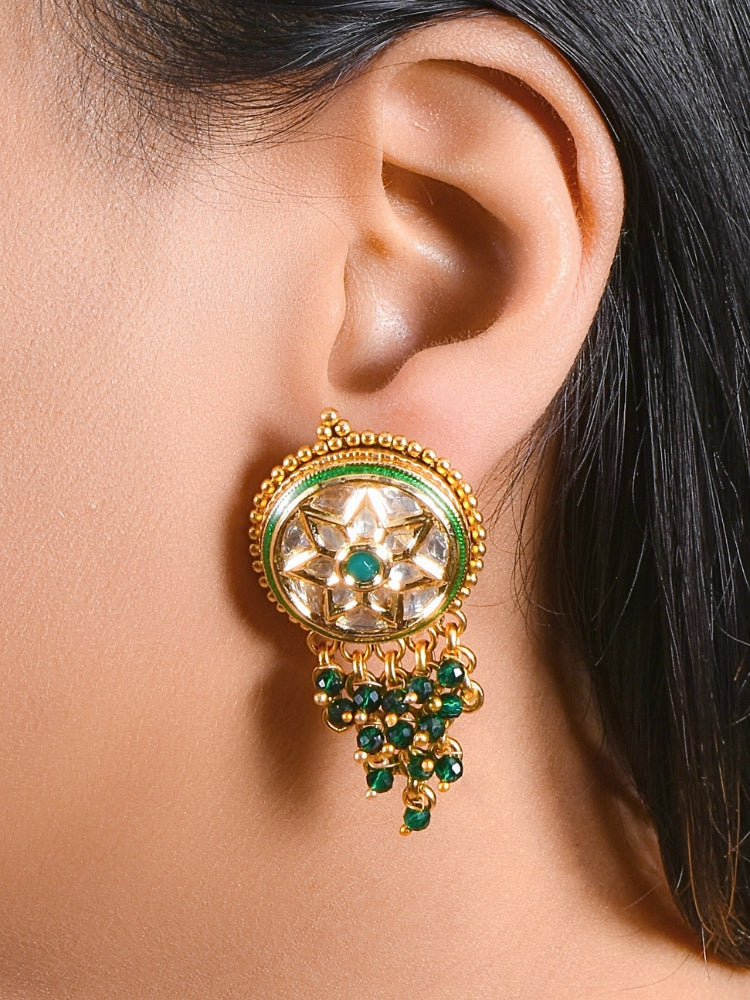 A close-up of a womans ear wearing Green Vartika Earrings—large, round gold earrings with tyani kundan, dangling green crystal beads, and American Diamond Polki—perfectly detailed for a wedding ceremony dress.