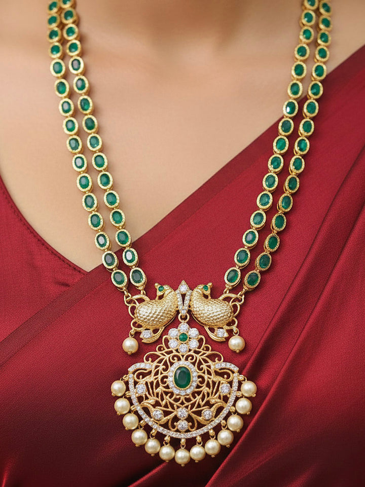 Close-up of a woman wearing an ornate traditional Green (gold Polish) Diamond jewellery set and earrings with American Diamond, Emerald Green Colored Stones and Pearls. A woman wearing a luxury American diamond necklace set styled beautifully for a wedding guest look in India. Model wearing a lightweight American diamond necklace perfect for long wedding functions.