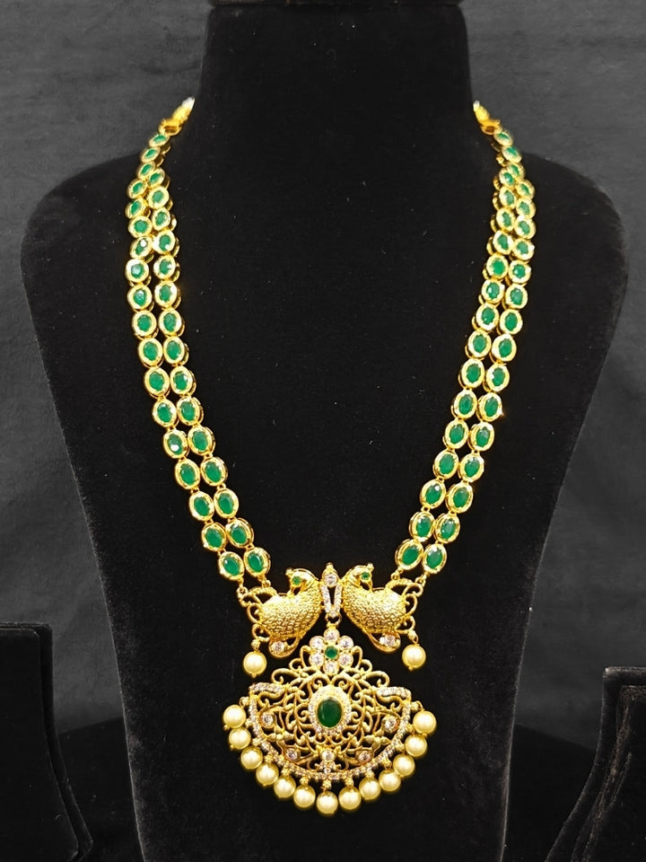 Close-up of an ornate traditional Green (gold Polish) Diamond jewellery set and earrings with American Diamond, Emerald Green Colored Stones and Pearls. A luxury American diamond necklace set styled beautifully for a wedding guest look in India. A lightweight American diamond necklace perfect for long wedding functions.
