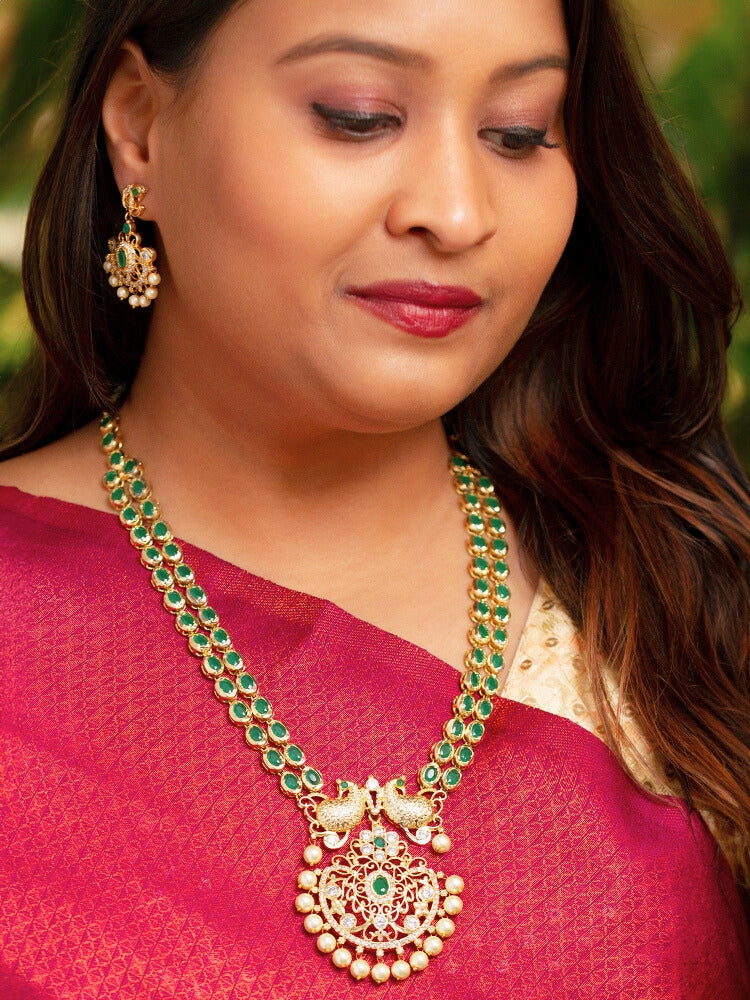 Close-up of a woman wearing an ornate traditional Green (gold Polish) Diamond jewellery set and earrings with American Diamond, Emerald Green Colored Stones and Pearls. A woman wearing a luxury American diamond necklace set styled beautifully for a wedding guest look in India. Model wearing a lightweight American diamond necklace perfect for long wedding functions.