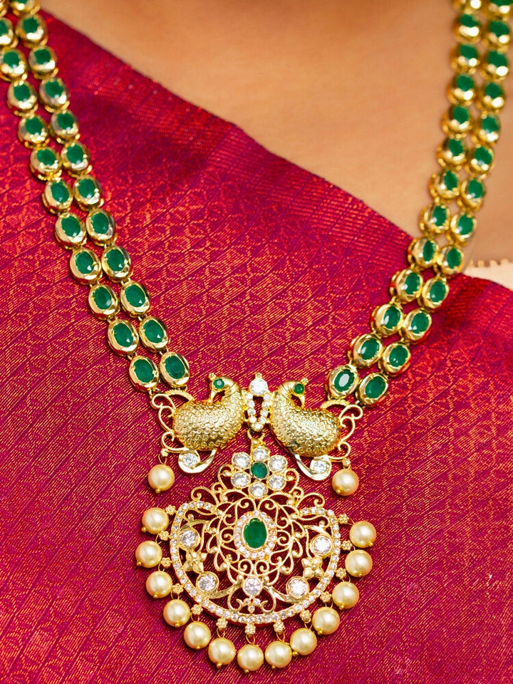 Close-up of a woman wearing an ornate traditional Green (gold Polish) Diamond jewellery set and earrings with American Diamond, Emerald Green Colored Stones and Pearls. A woman wearing a luxury American diamond necklace set styled beautifully for a wedding guest look in India. Model wearing a lightweight American diamond necklace perfect for long wedding functions.