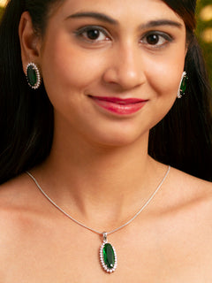 Close-up of a woman wearing an ornate Western (Silver Polish) Green Pendant set and Earrings with American Diamond and Green Colored Stone. Close-up of a cocktail party look featuring a premium Colored Stone Pendant Set. Party wear outfit completed with a lightweight Colored Stone Pendant set.