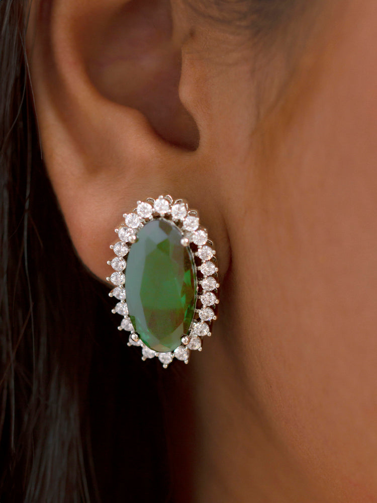 Close-up of a woman wearing an ornate Western (Silver Polish) Green Pendant set and Earrings with American Diamond and Green Colored Stone. Close-up of a cocktail party look featuring a premium Colored Stone Pendant Set. Party wear outfit completed with a lightweight Colored Stone Pendant set.