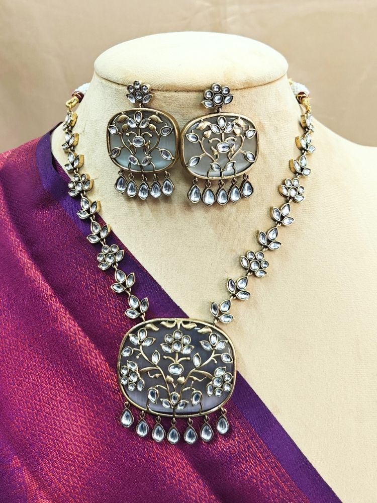 The Grey Bhavna Necklace Set is shown on a mannequin, featuring a necklace and matching earrings with floral motifs on a green base stone, Kundan embellishments on top, made in Mehendi polish, and dangling teardrop pearls.