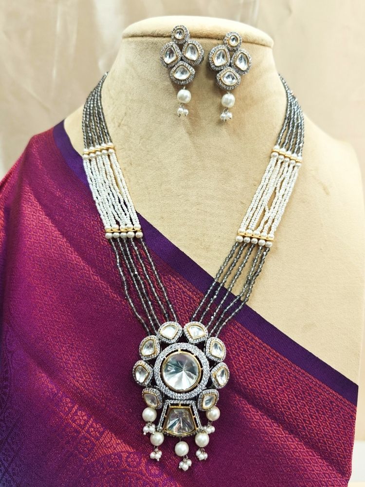 Grey Blair Necklace Set, featuring multi-strand crystals and pearls necklace, along with bog round and square tyani kundan stones, surrounded by american diamonds, along with pearls hanging at the bottom to accentuate the over all look. The necklace comes with matching earrings. shown on a Cream mannequin. 