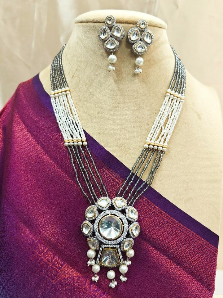 Grey Blair Necklace Set, featuring multi-strand crystals and pearls necklace, along with bog round and square tyani kundan stones, surrounded by american diamonds, along with pearls hanging at the bottom to accentuate the over all look. The necklace comes with matching earrings. shown on a Cream mannequin. 