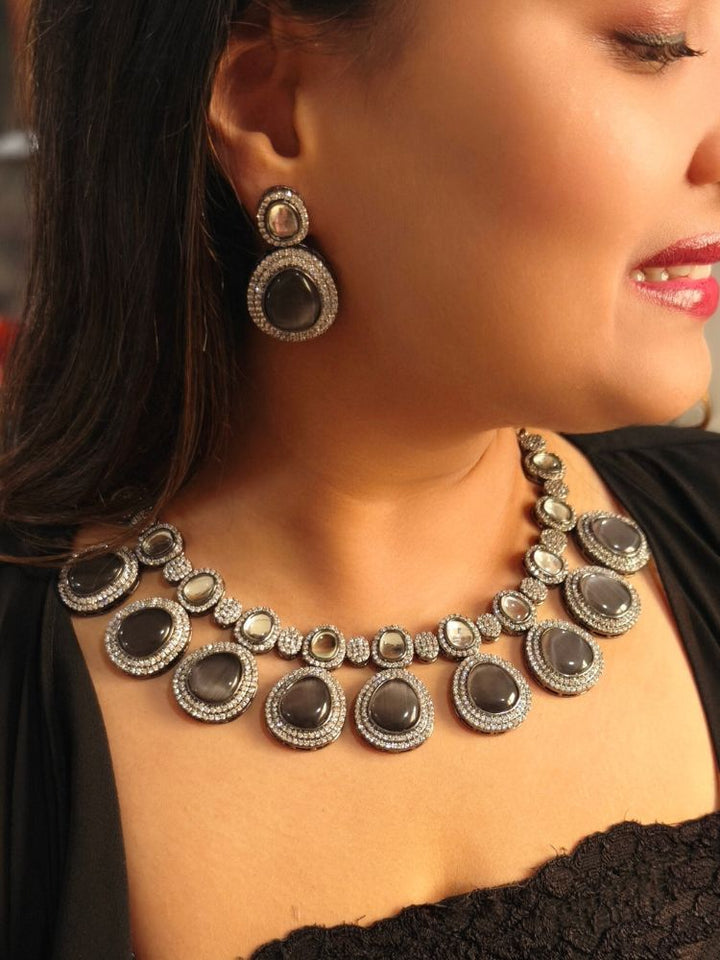 A woman with brown hair down smiles to the side, wearing the Grey Elizabeth Necklace Set featuring a statement Victorian-style necklace and matching earrings with large colorful stones, paired with a sparkly dark top.